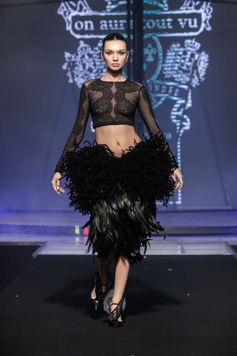 A model walking on aura tout vu couture show black lace top and feathers ans sequenses embroidered black skirt