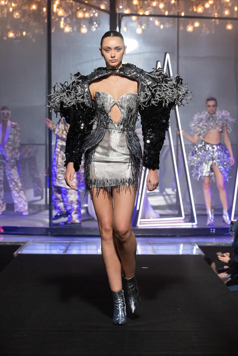 A model walk on aura tout vu show wearing silver jacket and silver fringes.