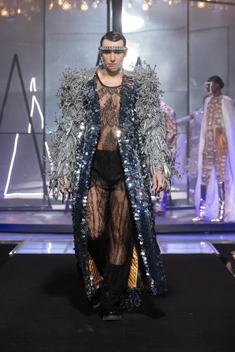 A male model walk on aura tout vu show wearing silver coat top and pants in black lace