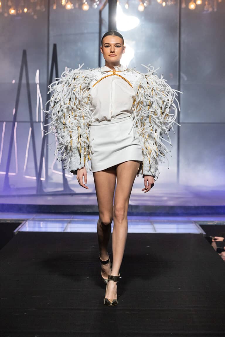 a model walking the on aura tout vu show wearing kobe leather skirt and embroidered white bolero