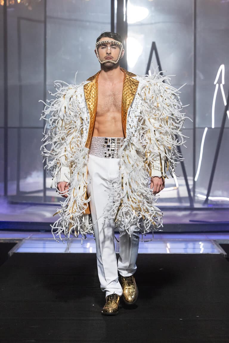 A male model walk on aura tout vu show wearing white embroidered with spikes coat and white pants