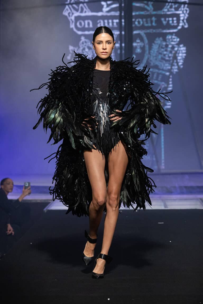 A model walk on aura tout vu show wearing black bodysuit long coat embroidered with sequins and feathers