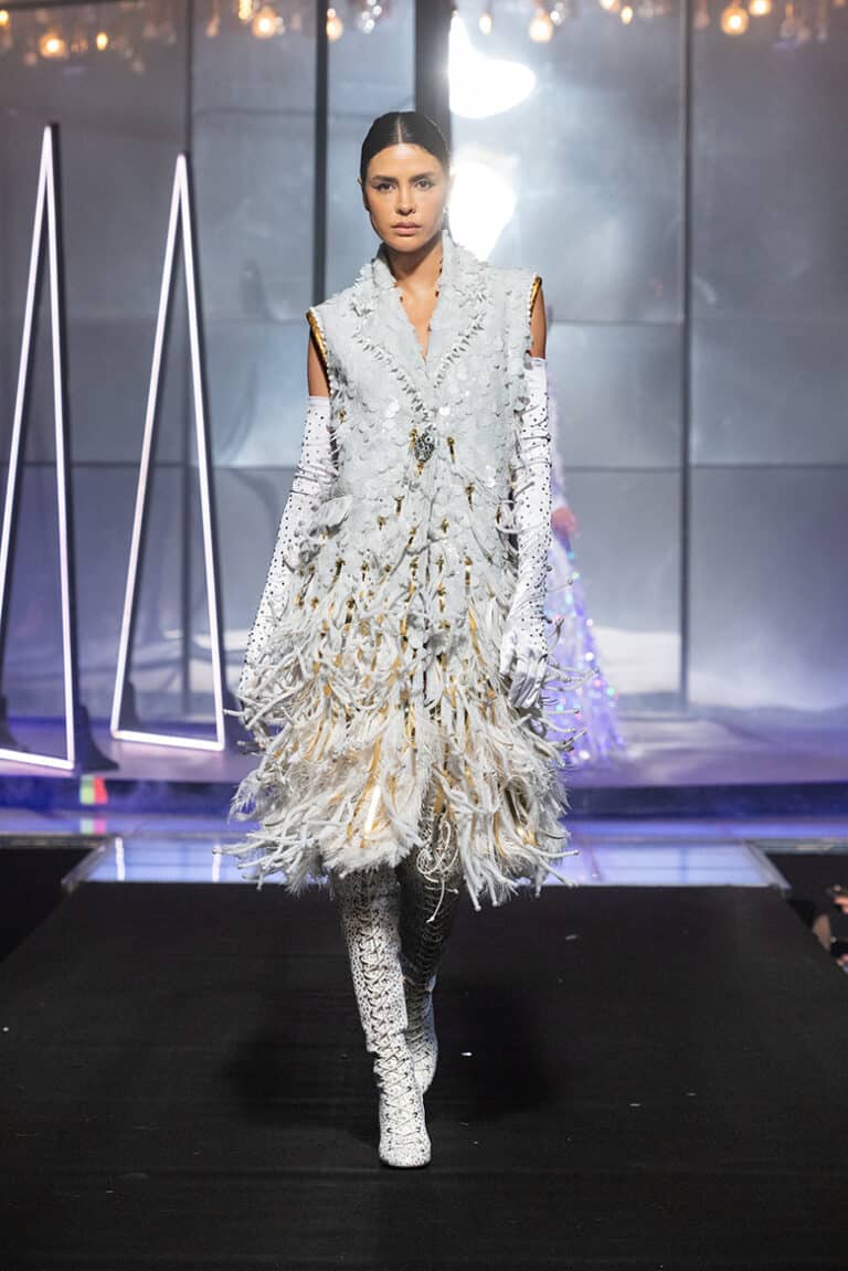 a model walking the on aura tout vu show wearing white and gold coat