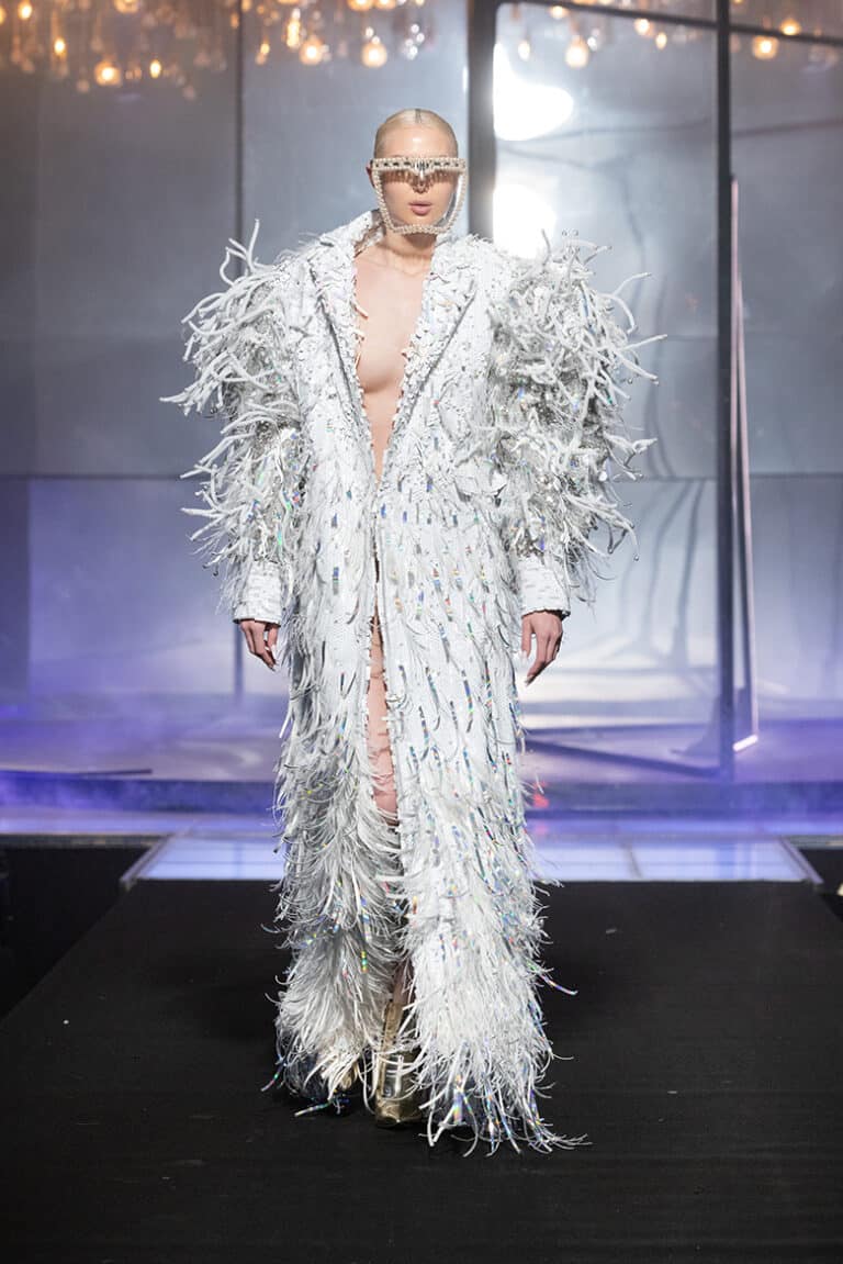 a model walking the on aura tout vu show wearing white and gold coat