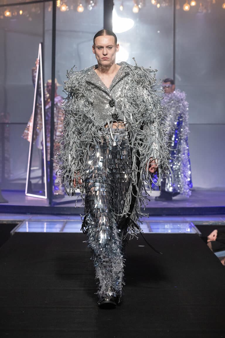 A male model walk on aura tout vu show wearing silver jacket and silver fringes.